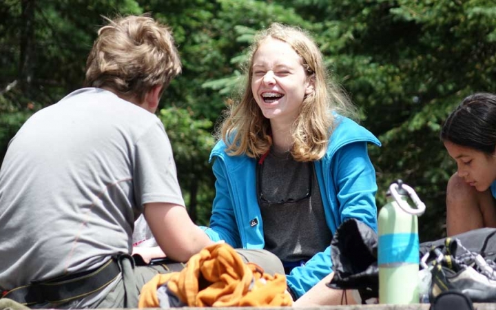 teens laugh as they pack a backpacking on an outdoor leadership course